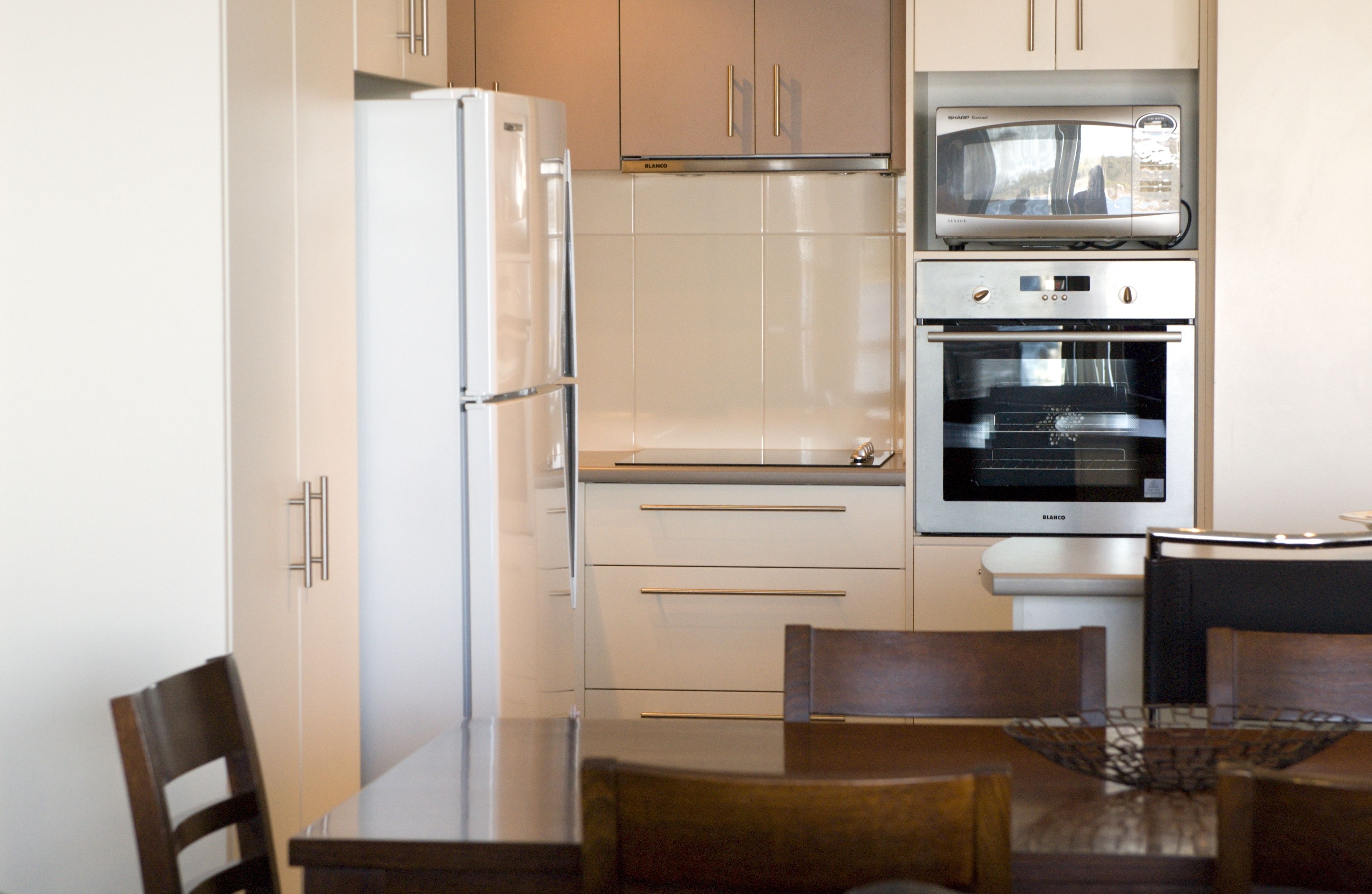 A modern kitchen with a refrigerator, microwave, oven, and a dining table with chairs.