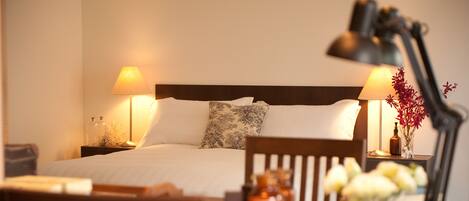 A neatly arranged hotel room with a bed, two bedside lamps, a nightstand, a chair, a table with a book and a vase of flowers.