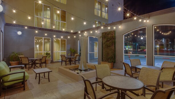 An outdoor patio with wicker furniture, string lights, and large windows offering views of the street. - Fairfield Inn & Suites by Marriott San Francisco Airport (Millbrae)