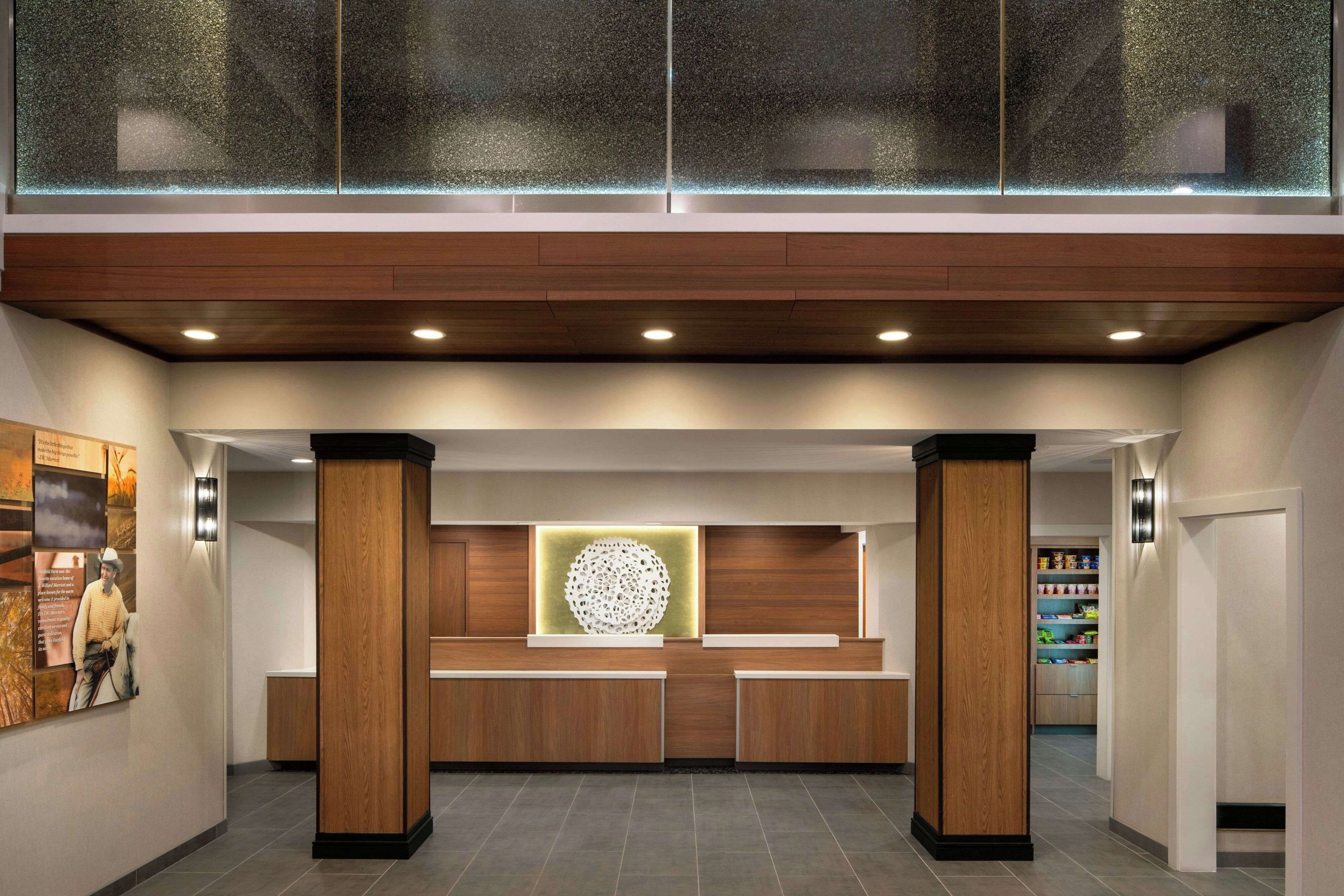 A reception area with a wooden reception desk, a decorative wall piece, and a glass partition above.
