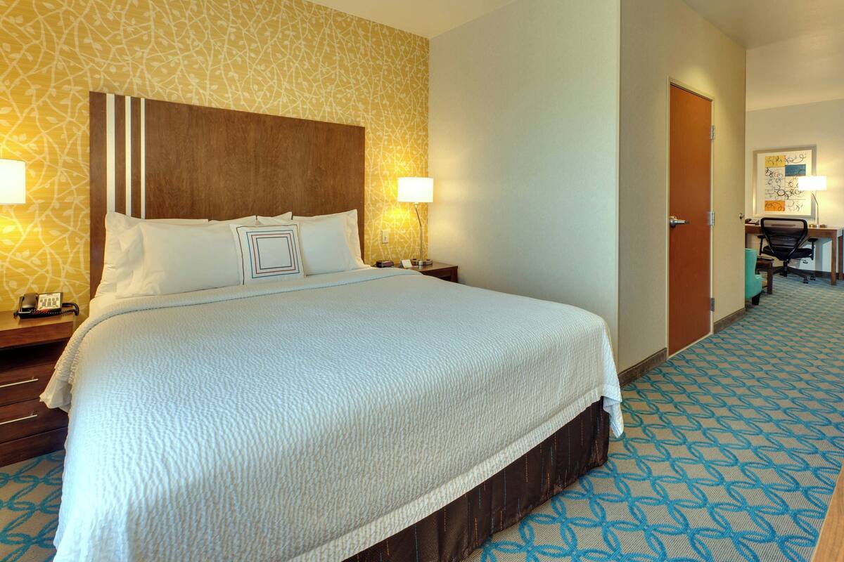 Een hotelkamer met een groot bed, twee nachtkastjes, een bureau met stoel en een kamerbreed tapijt met een patroon.
