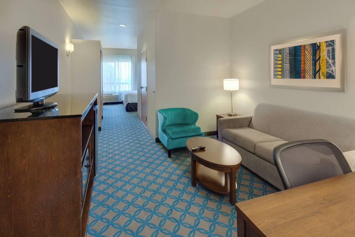 Een hotelkamer met een televisie, een bank, een blauwgroene fauteuil, een bijzettafeltje en een schilderij aan de muur.