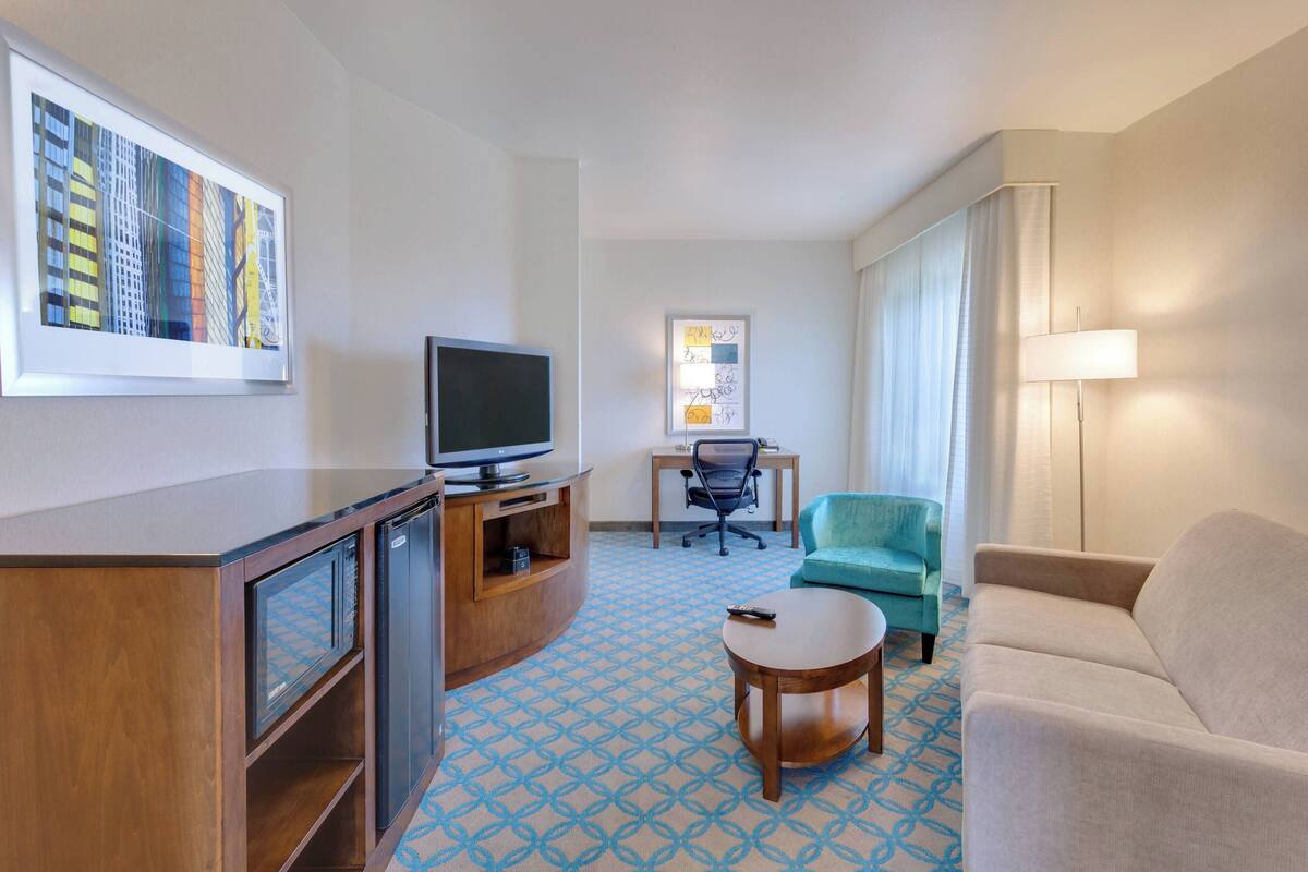 Een hotelkamer met een televisie, bureau, stoel, bank en een kamer met een patroon.