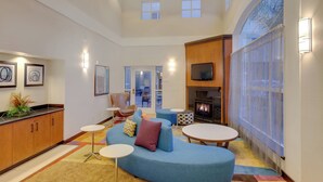 A modern living room with a curved blue sofa, a fireplace, and a large window with sheer curtains. - Fairfield Inn & Suites by Marriott San Francisco Airport (Millbrae)