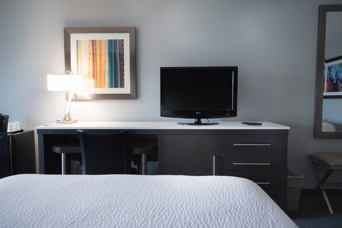 Hotelkamer met een bed, een bureau met een televisie, een lamp en een ingelijst schilderij aan de muur.