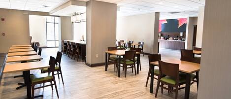 A spacious dining area with multiple tables and chairs, a counter with a display, and a large window providing natural light.