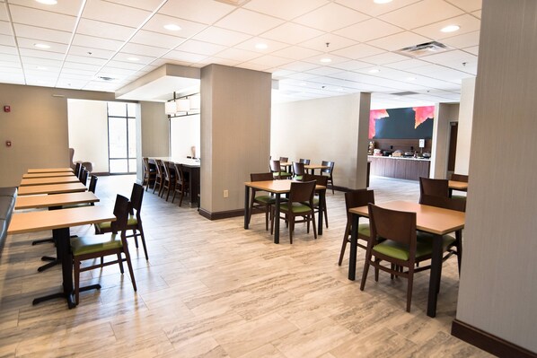 A spacious dining area with multiple tables and chairs, a counter with a display, and a large window providing natural light.