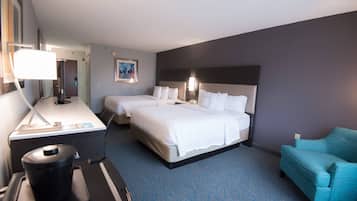 A hotel room with two beds, a desk, a chair, and a trash bin.