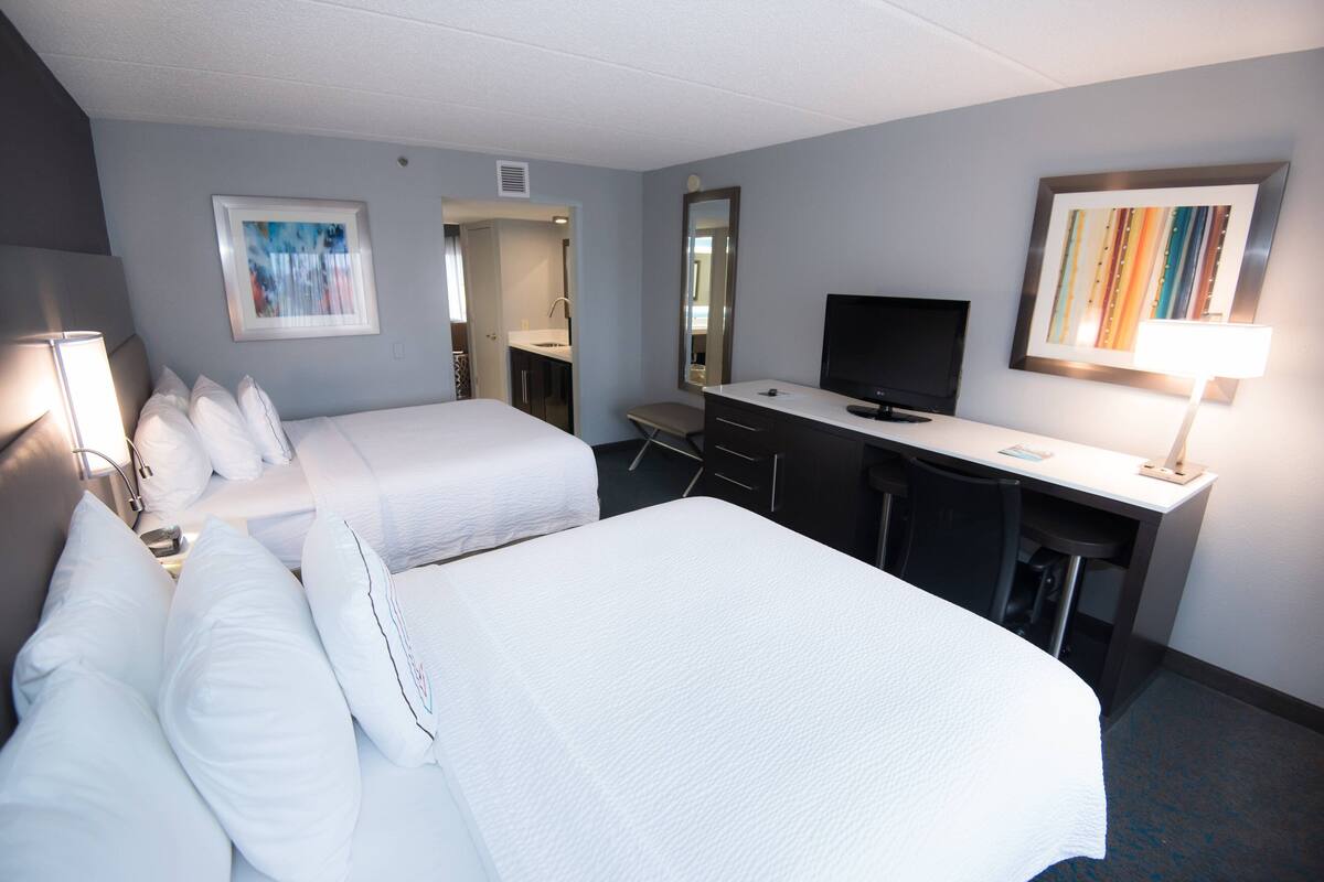 Een hotelkamer met twee bedden, een bureau met een computer, een televisie en een badkamer die door een open deur zichtbaar is.
