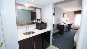 Une chambre d’hôtel équipée d’une kitchenette, d’un évier, d’un four à micro-ondes, d’un petit réfrigérateur, d’un bureau avec une chaise et d’un lit.