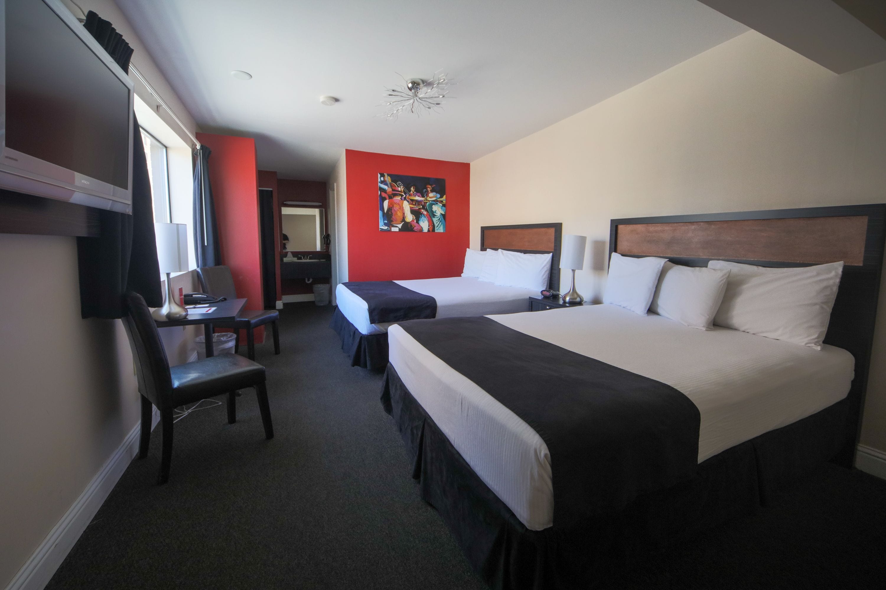 A hotel room with two beds, a desk, a chair, and a TV.