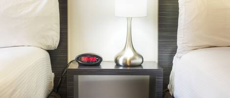 A hotel room with a bed, a nightstand, a lamp, and a digital clock.