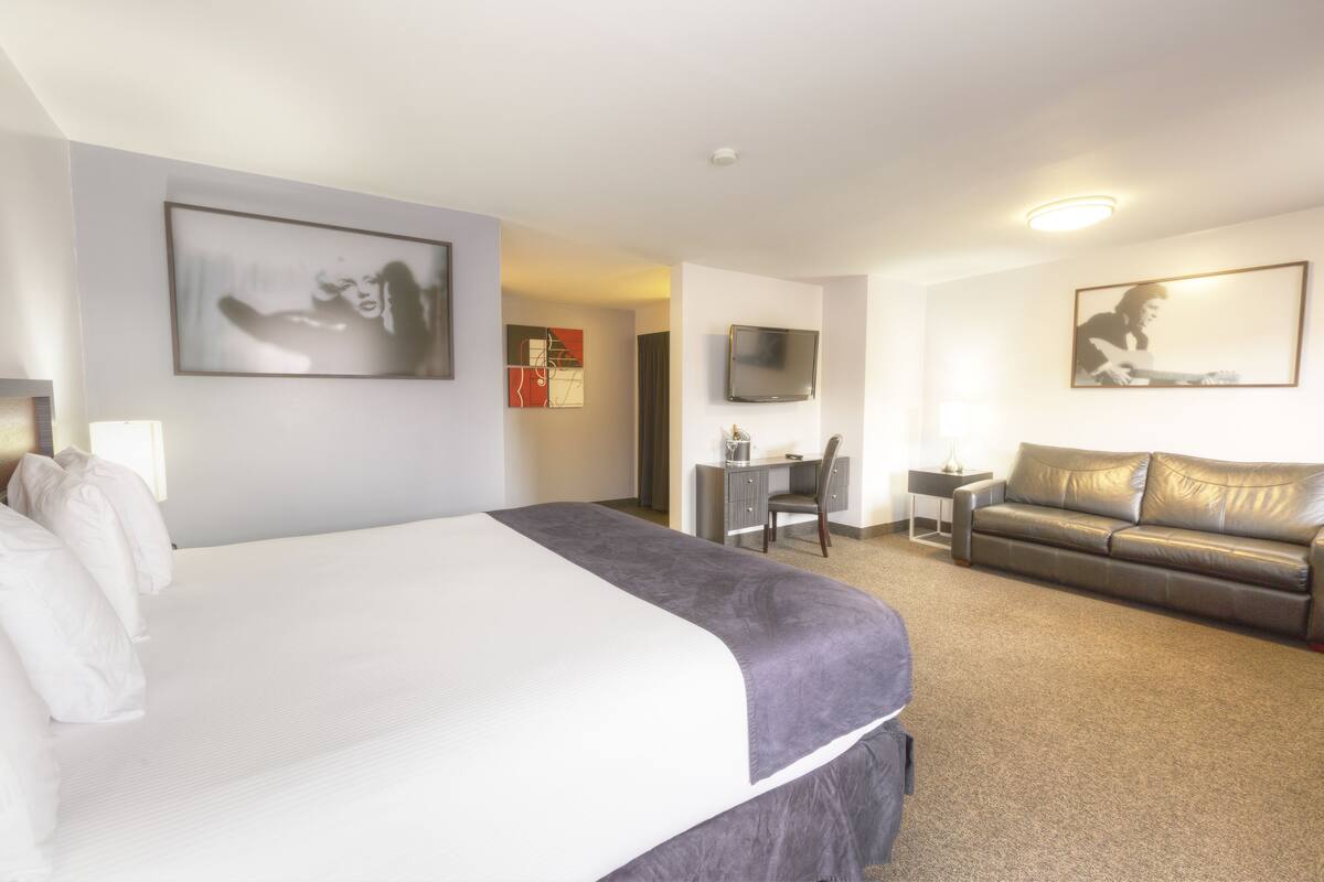 A hotel room with a large bed, a desk, a leather sofa, and a TV on the wall.