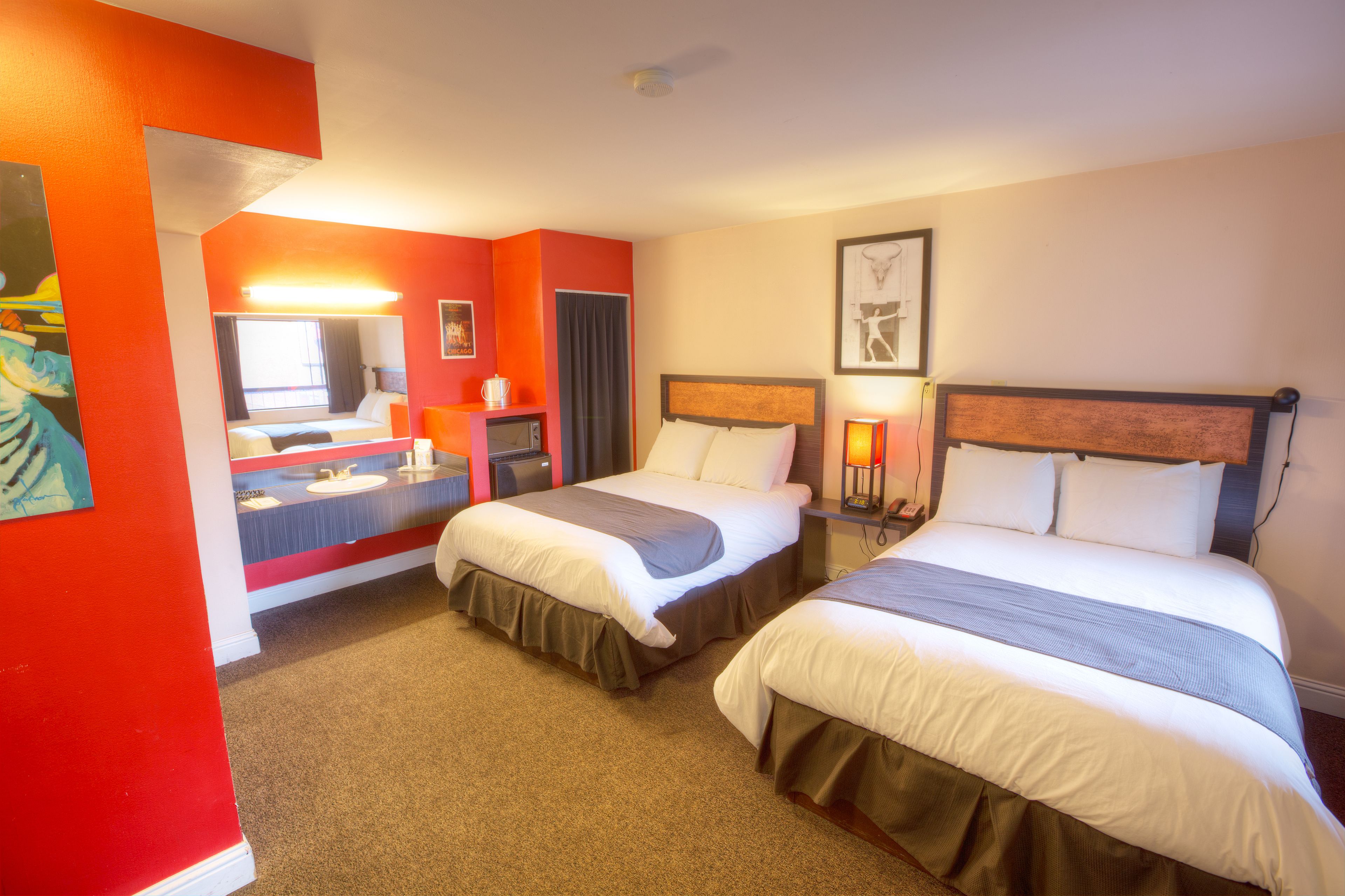 A hotel room with two beds, a bathroom with a mirror, and a painting on the wall.