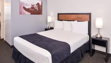 A neatly made bed with white and dark bedding, two bedside tables with lamps, and a framed picture on the wall.