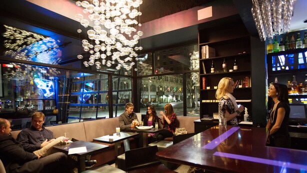 A modern bar with leather seating, a bar counter, and a large window offering a city view. - Hotel Ruby (Spokane)