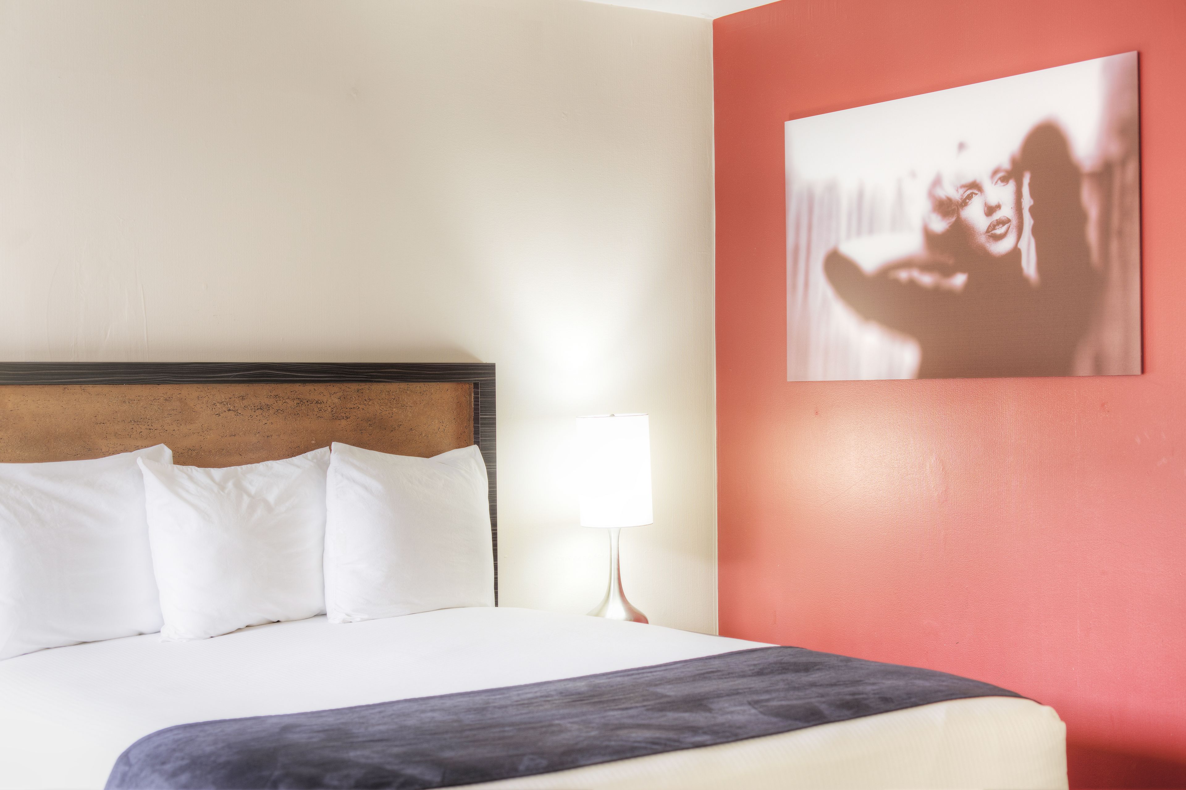 A neatly made bed with white bedding and a dark throw blanket, a wooden headboard, and a single bedside lamp.
