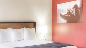 A neatly made bed with white bedding and a dark throw blanket, a wooden headboard, and a single bedside lamp.