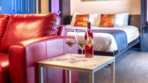 A hotel room with a red leather sofa, a bed with patterned pillows, and two glasses of red wine on a small table. - Hotel Ruby (Spokane)