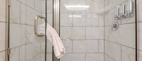 A shower with a glass door, marble tiles, a towel rack, and a wall-mounted hand dryer.