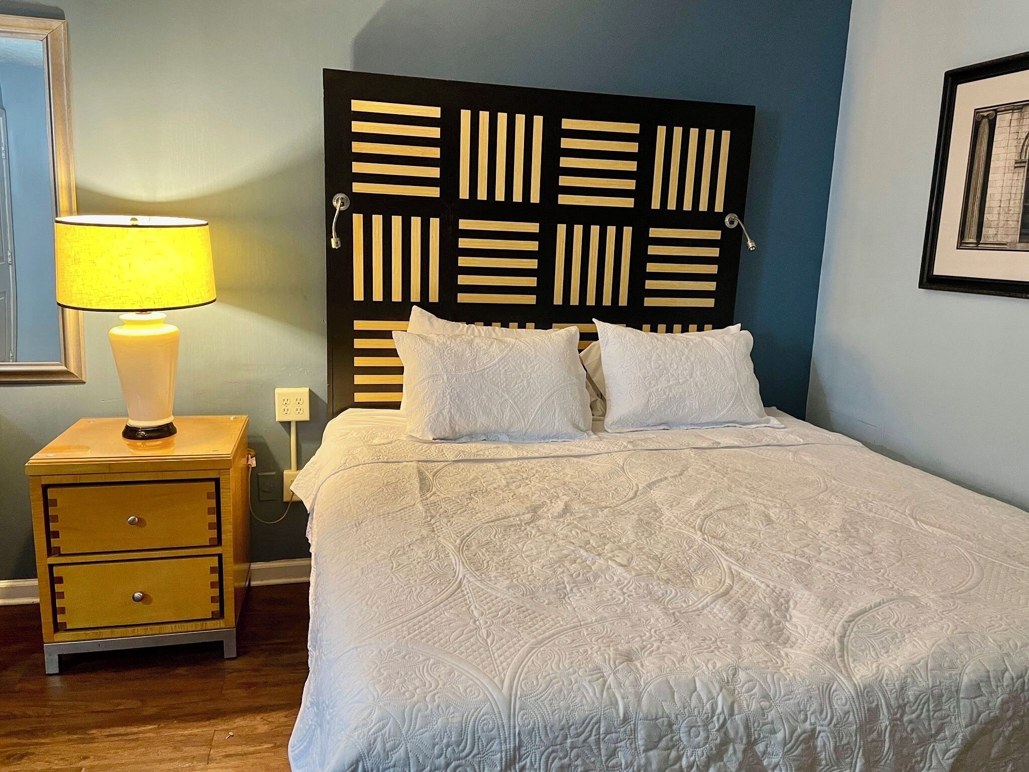 A neatly made bed with a patterned bedspread, a bedside lamp, and a wooden nightstand with drawers.
