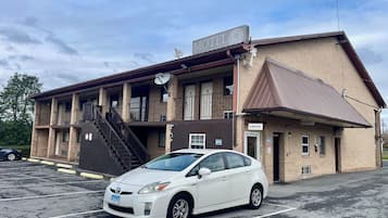 Un motel de una sola planta, con una escalera que lleva a la entrada y un coche blanco estacionado al frente.