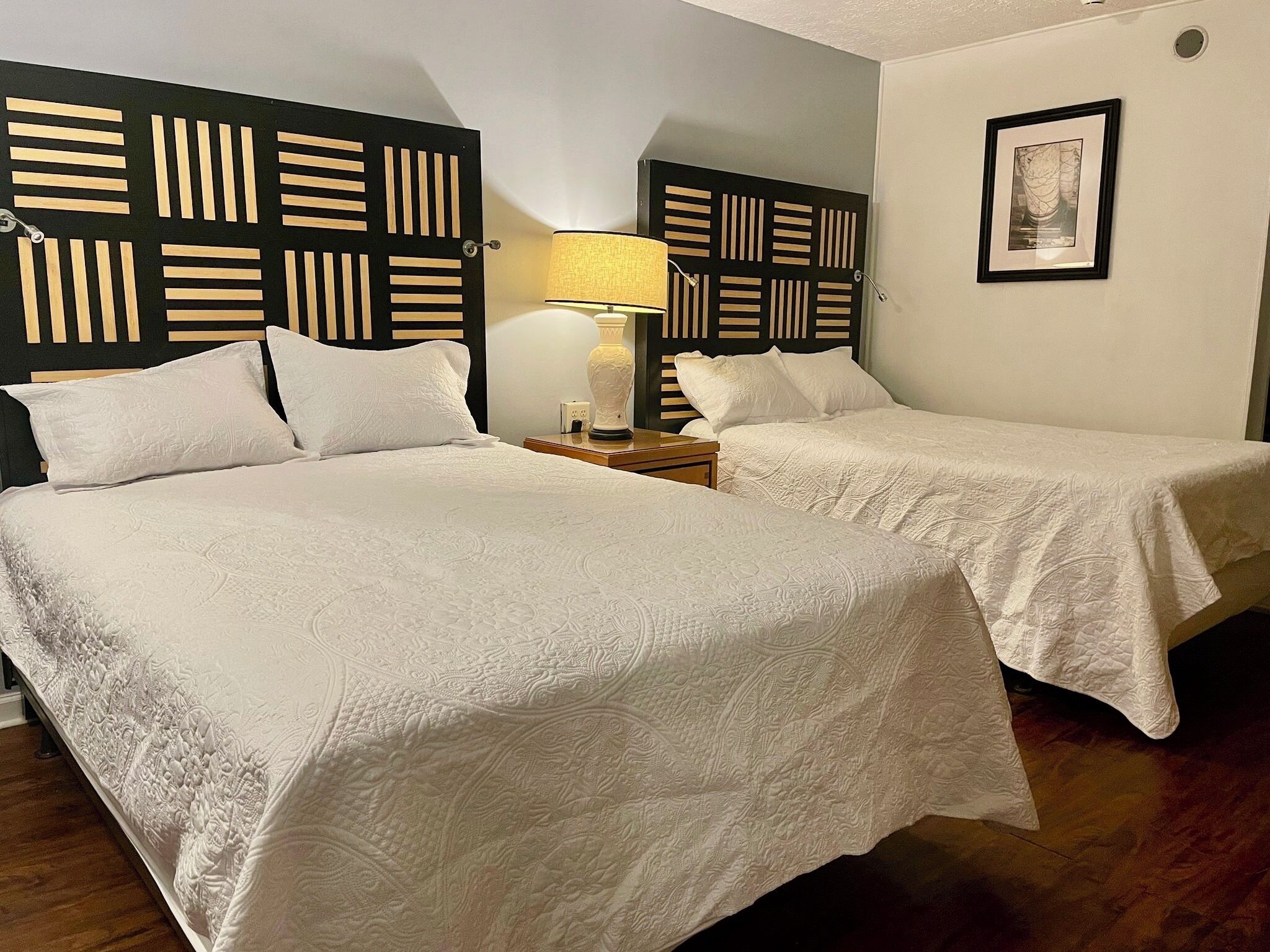 A hotel room with two beds, a nightstand with a lamp, and a framed picture on the wall.