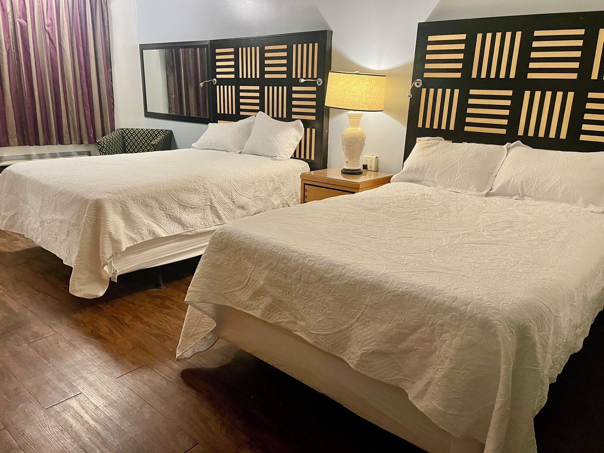 Een hotelkamer met twee bedden, houten hoofdeinden, een nachtkastje met lamp en een grote spiegel.