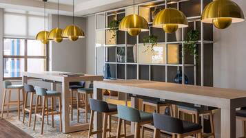 A modern bar area with wooden stools and a long table, surrounded by a patterned rug and pendant lights.