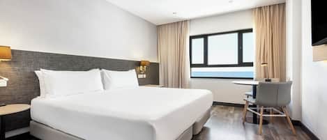 Habitación de hotel con una cama grande, un escritorio con silla, ventana con vistas y un televisor montado en la pared.