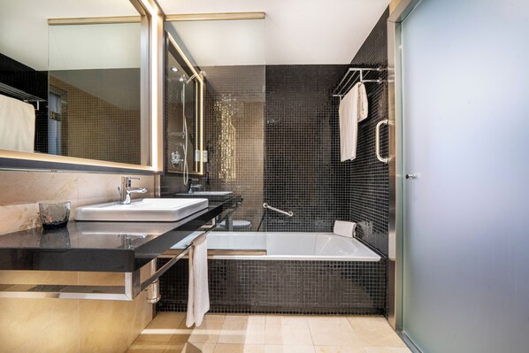 A modern bathroom with a large mirror, two sinks, a bathtub, and a glass shower enclosure.