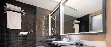 Un baño moderno con ducha de vidrio, lavamanos sobre encimera negra y un espejo grande.