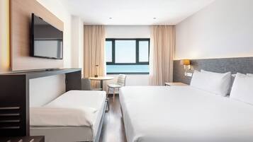 Habitación de hotel con dos camas, televisión, escritorio con silla, lámpara y vista al mar.