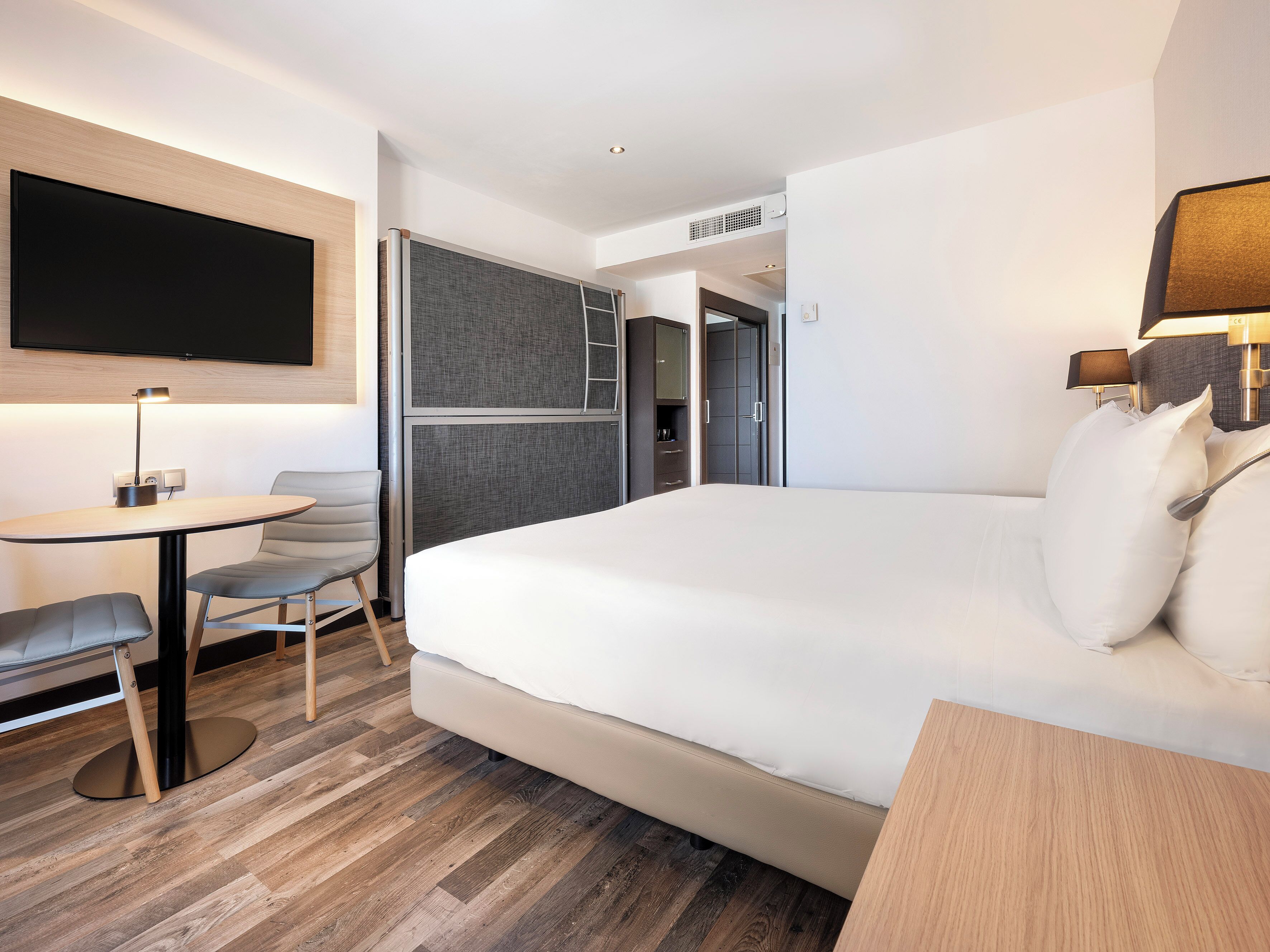 Habitación de hotel moderna con una cama grande, un escritorio con una silla, un televisor de pantalla plana en la pared y un armario con espejo.
