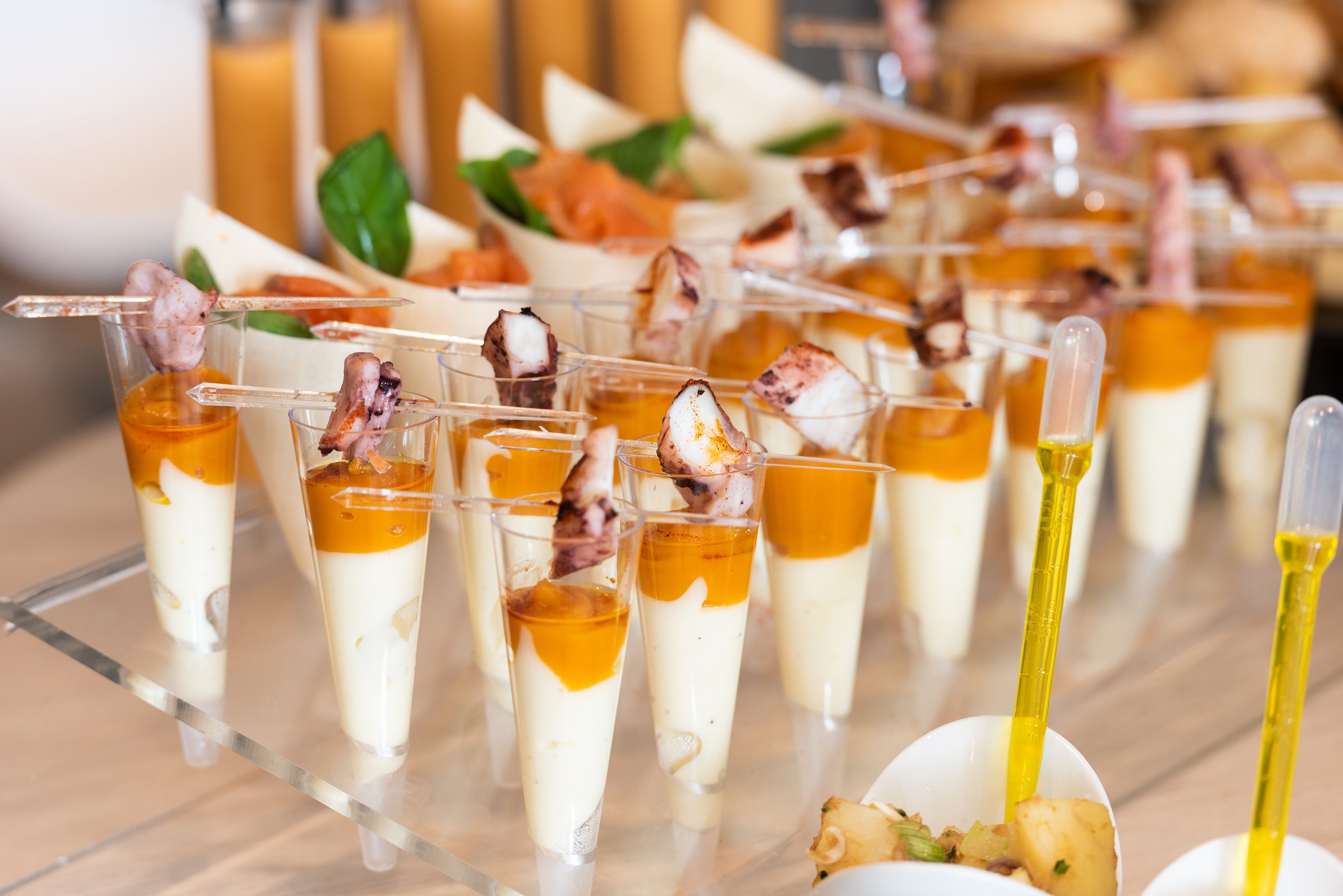 A variety of appetizers including skewered seafood and a dessert with a golden syrup layer, served on a glass tray.