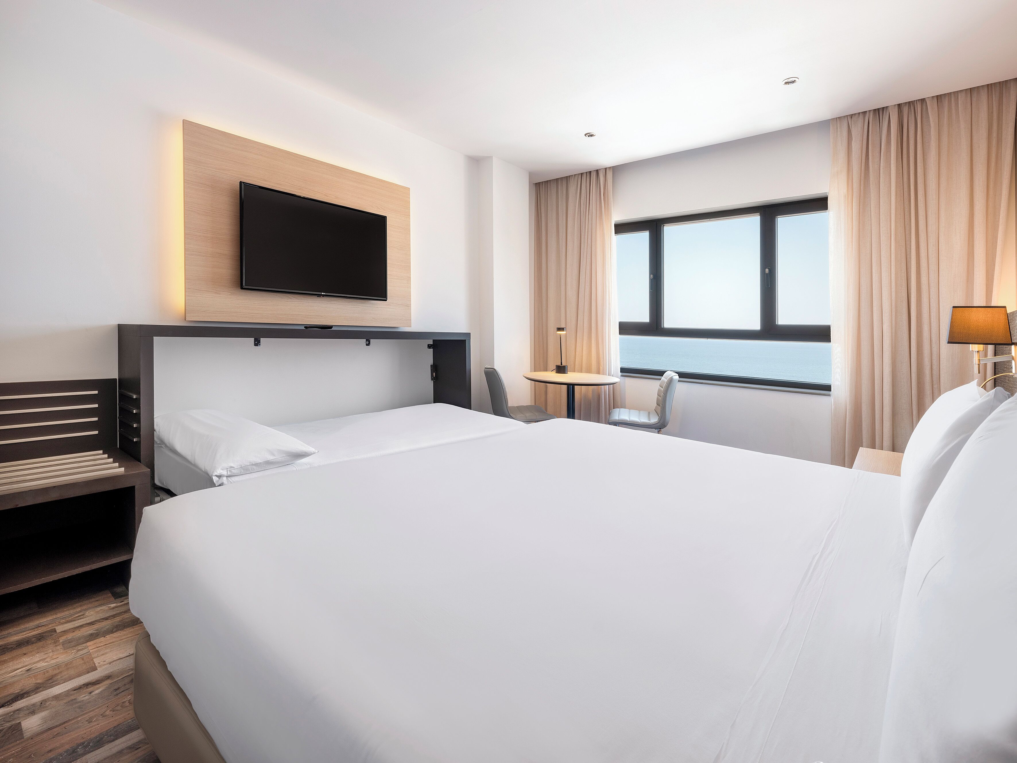 Une chambre d’hôtel avec un grand lit, un bureau, une chaise, un téléviseur fixé au mur et une fenêtre avec des rideaux.