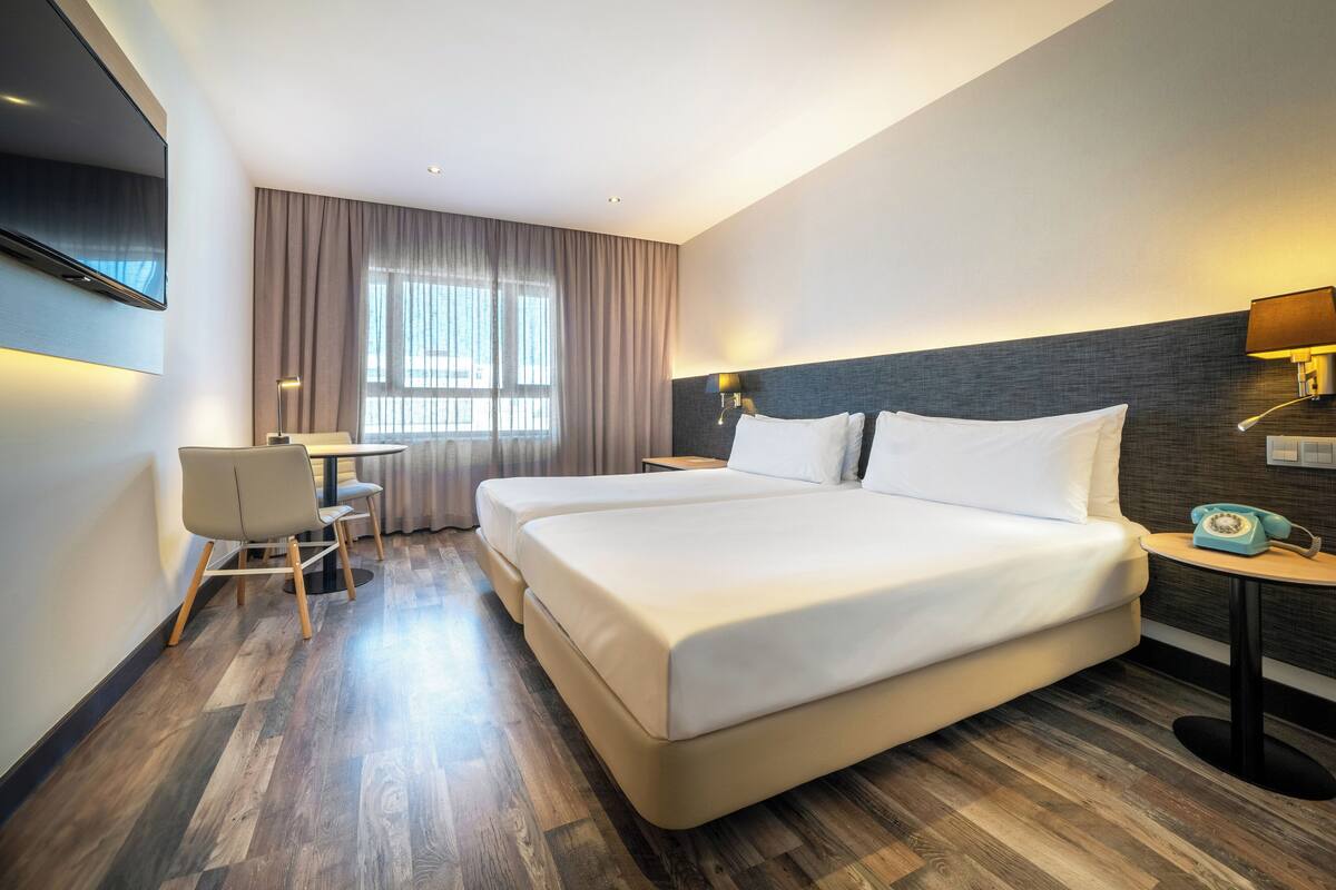 A hotel room with a large bed, a desk, a chair, and a television.