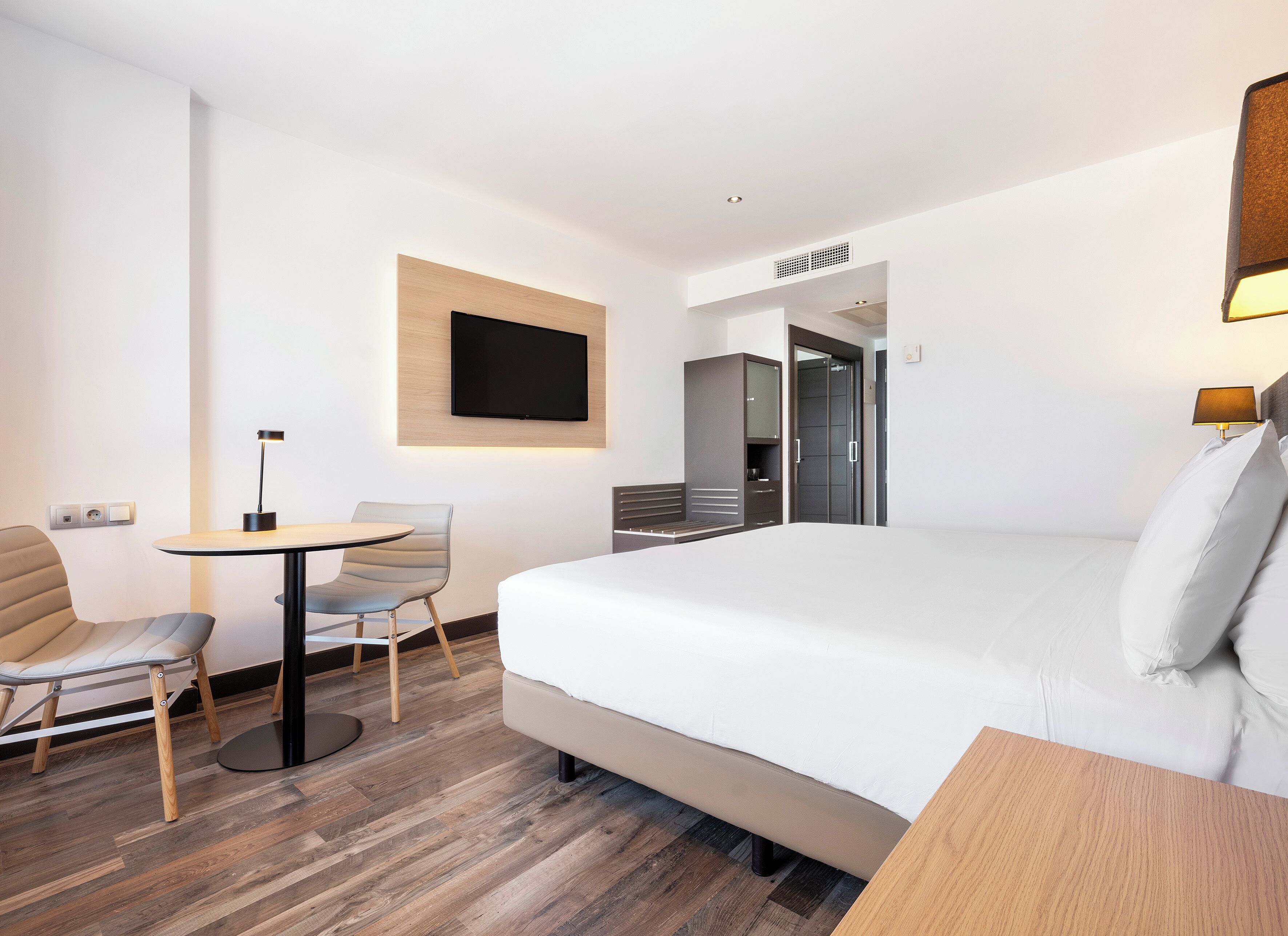 Habitación de hotel con cama, escritorio, silla, televisor montado en la pared y armario.