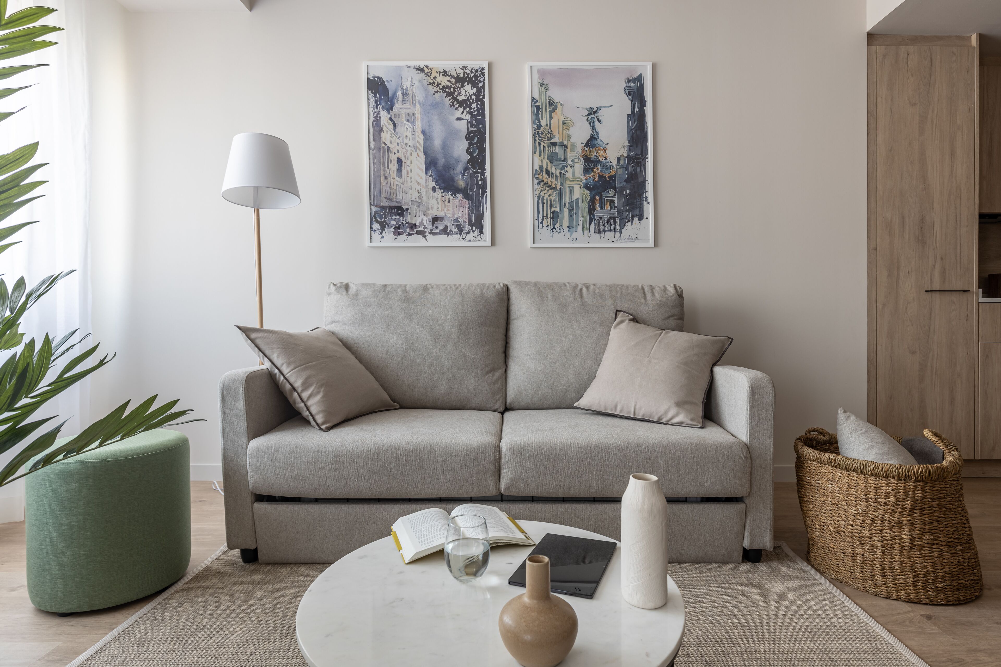 Una sala de estar moderna con un sofá gris, dos mesitas auxiliares, una lámpara de pie y una gran planta en maceta.