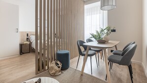 A modern hotel room with a wooden partition, a dining area with a round table and chairs, a bed, and a bedside table with a lamp. - Líbere Madrid Chamberí (Madrid)
