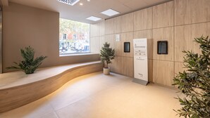 A modern reception area with a curved bench, potted plants, a check-in kiosk, and a view of the street outside.