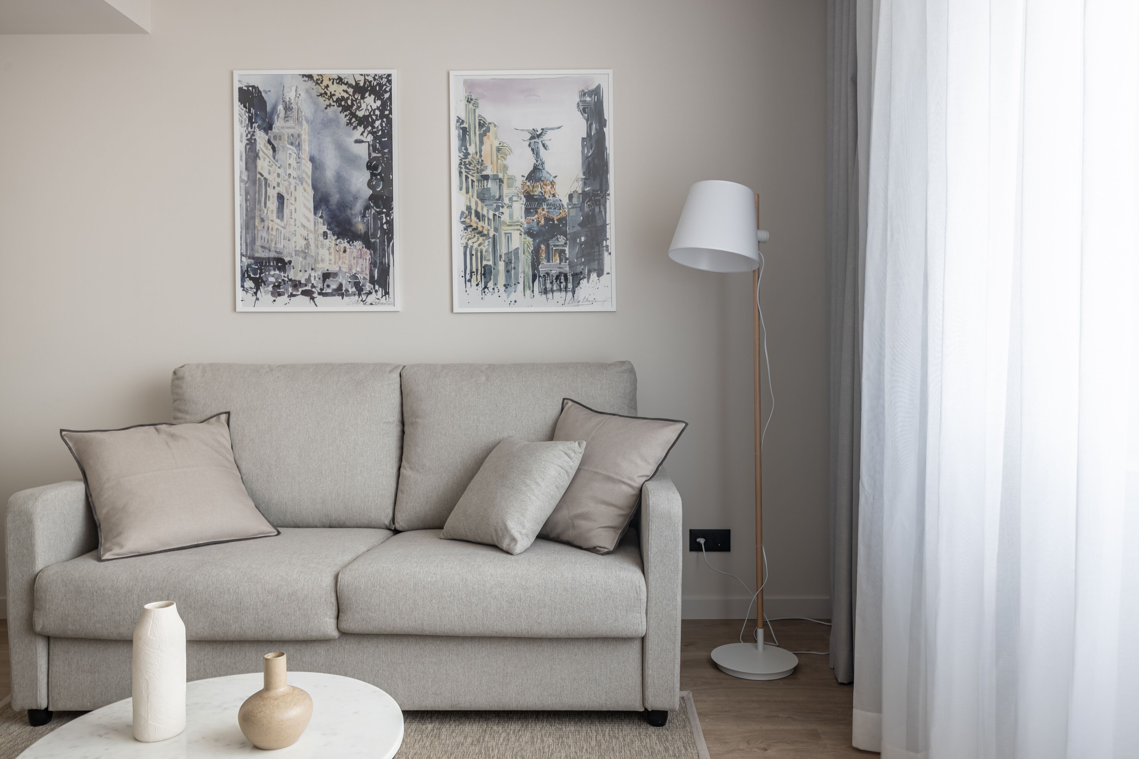 Ein modernes Wohnzimmer mit einem grauen Sofa, zwei Kissen, einer weißen Vase und einer Stehlampe.