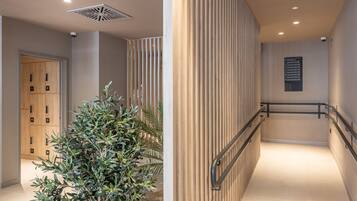 Un pasillo moderno de hotel con una puerta de madera, una planta, un panel de madera vertical y un letrero con números de habitaciones.