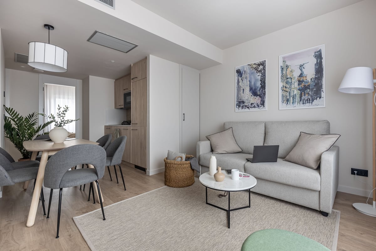 A modern living room with a grey sofa, a dining table with chairs, and a kitchen area in the background.