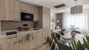 A modern kitchen with wooden cabinets, a black microwave, and a sink. There is a dining area with a table and chairs, and a large window with curtains. - Líbere Madrid Chamberí (Madrid)