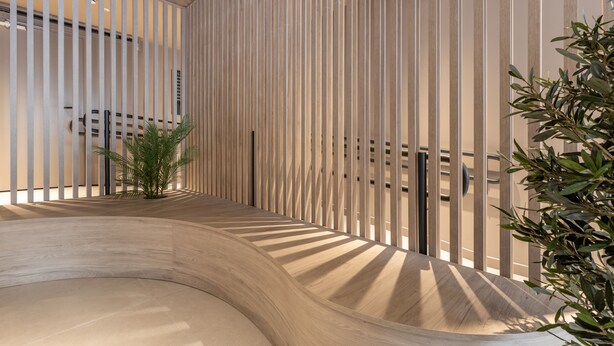 A modern interior with vertical wooden slats, a curved wooden bench, and a small plant. - Líbere Madrid Chamberí (Madrid)
