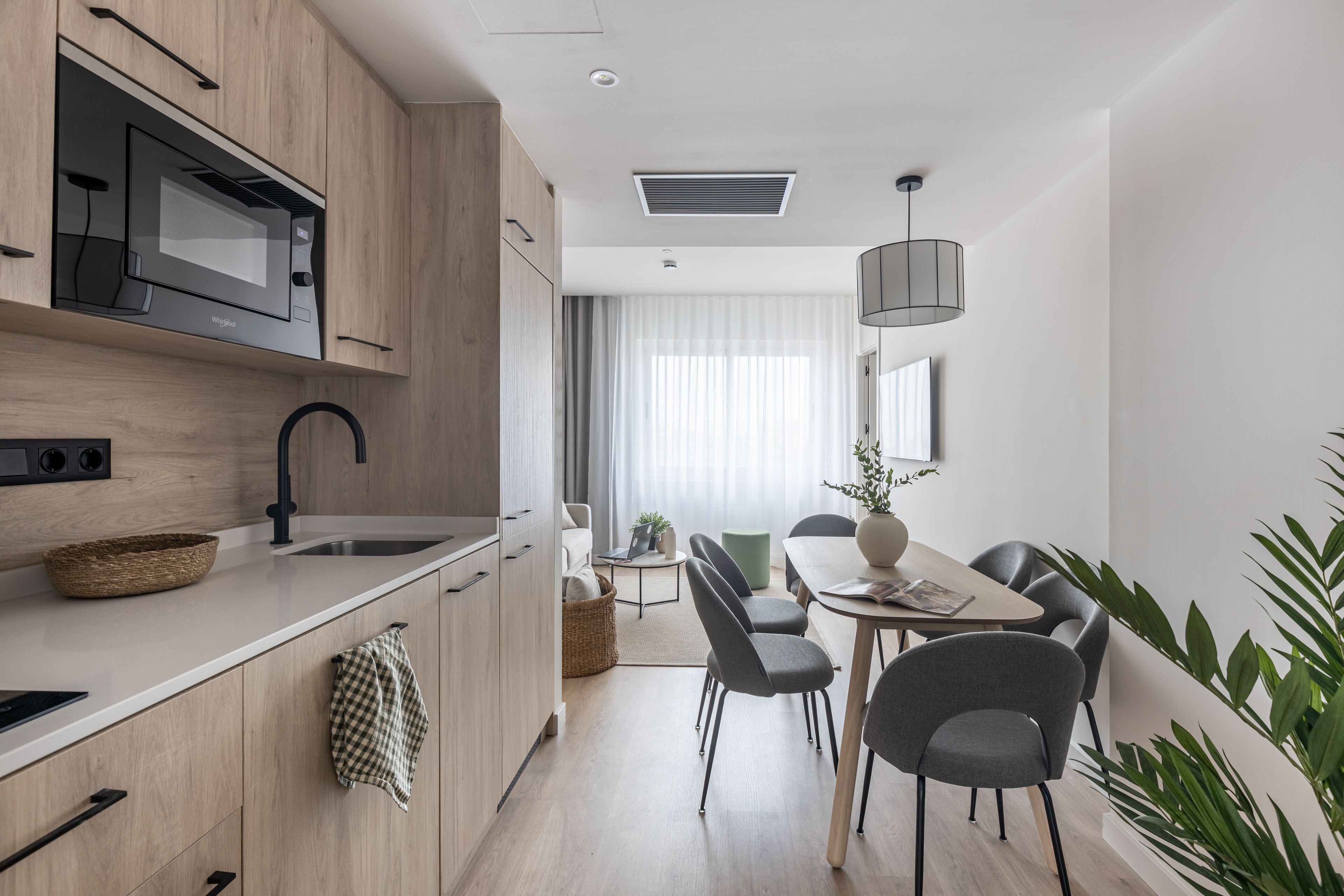 Una cocina moderna con microondas integrado, un lavamanos y una zona de comedor con mesa y sillas.