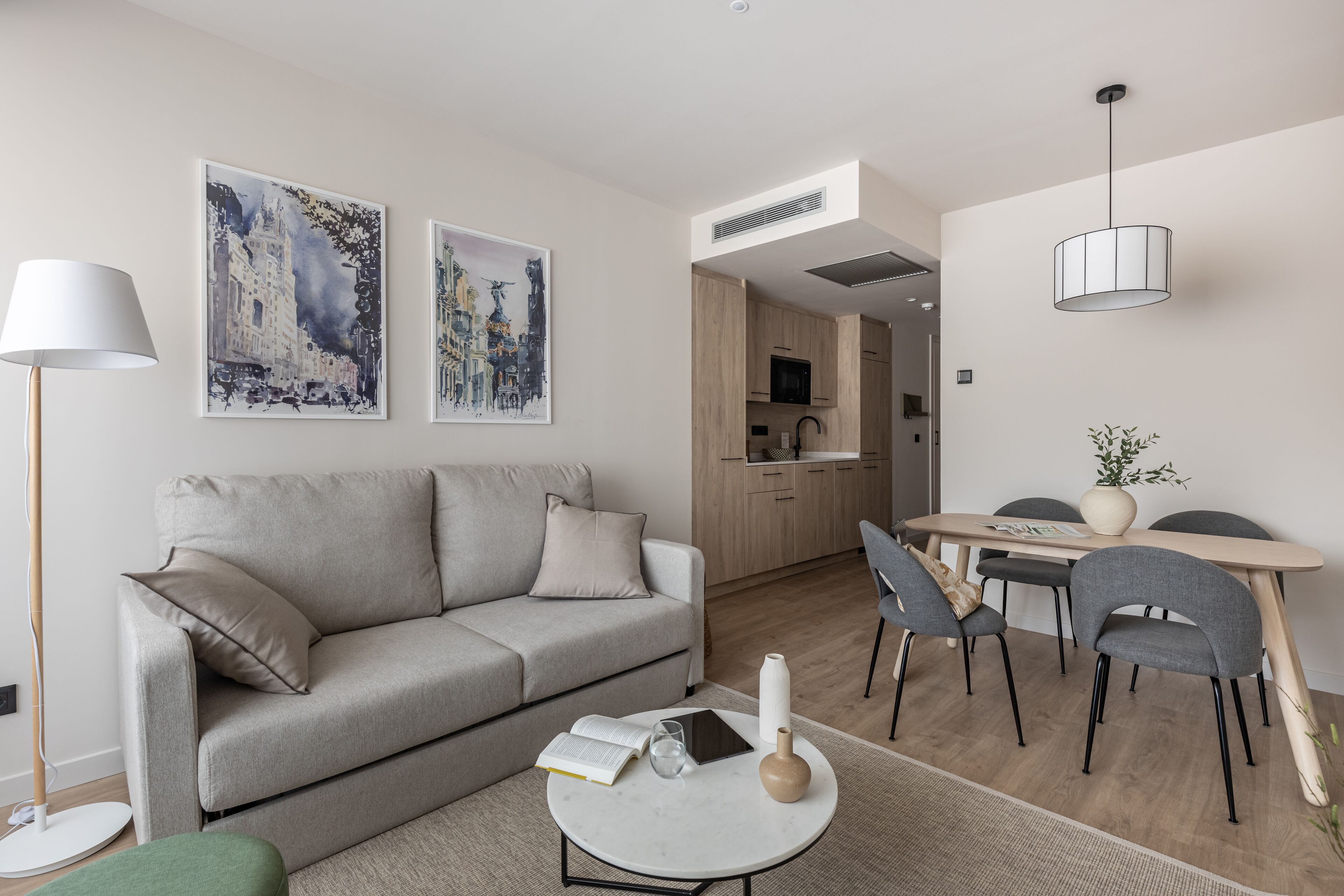 A modern living room with a sofa, a dining table with chairs, and a kitchen area.