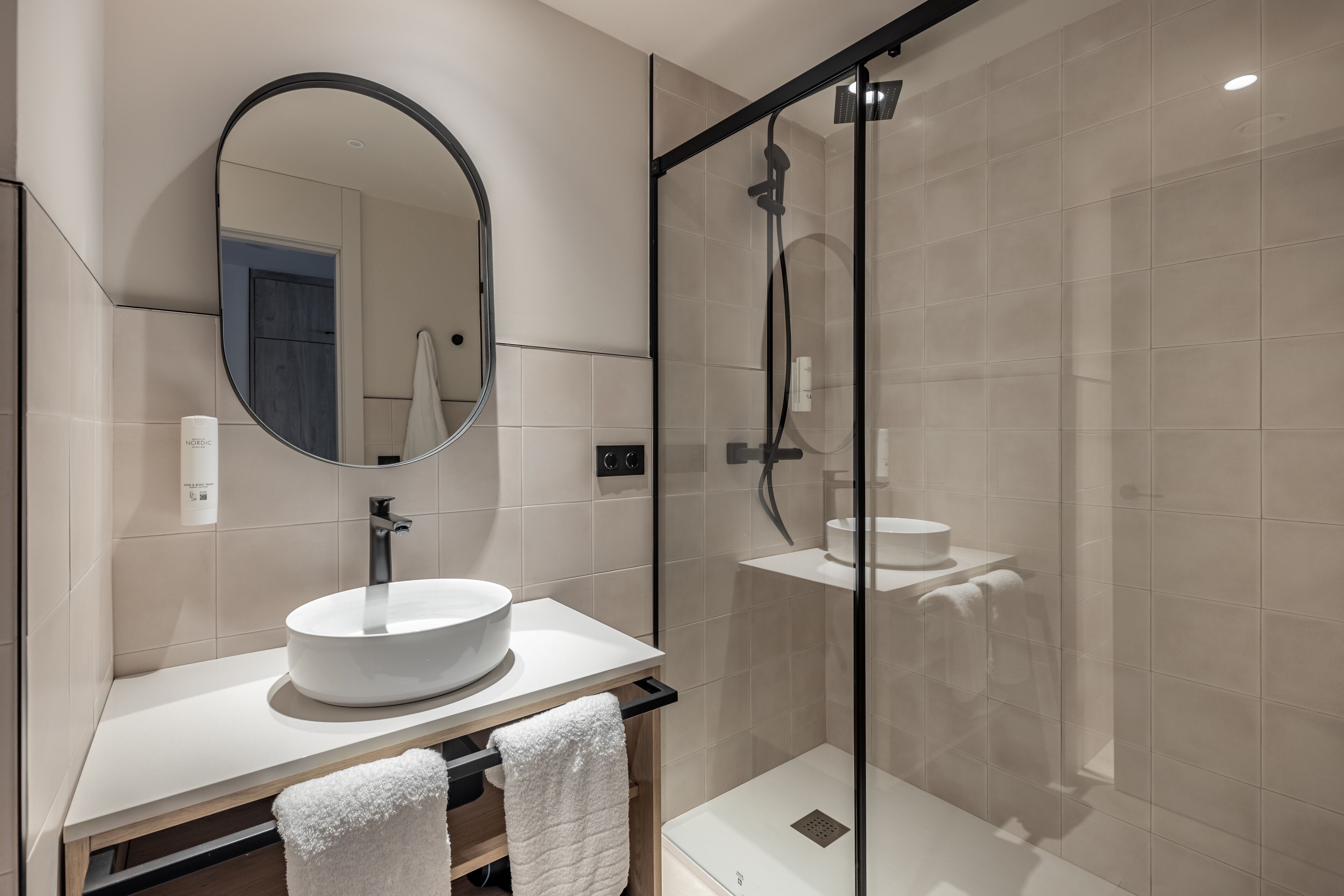 A modern bathroom with a round mirror, a white sink, and a glass-enclosed shower.