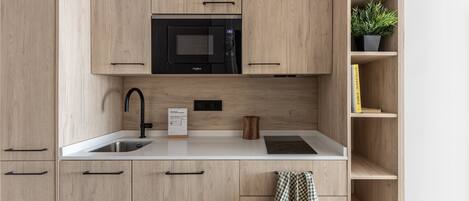 A modern kitchen with wooden cabinets, a black microwave, a sink, and a potted plant on a shelf.